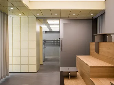 現代極簡玄關展示淺色橡木樓梯、嵌入式長椅、淡黃色穿孔牆板、混凝土地板，以及通往不鏽鋼元素廚房區域的視野。