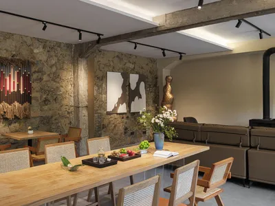 現代工業風餐廳，擁有裸露石牆、長型淺橡木餐桌、木製藤編椅、棕色皮革沙發與當代藝術作品。