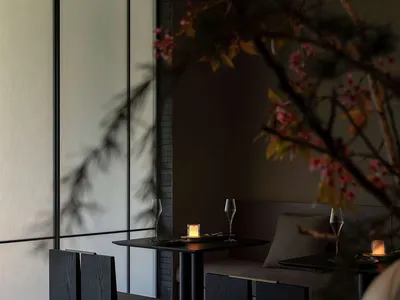 Modern dark oak dining room featuring built-in banquette seating, black dining table, and glowing candles with large windows in the background.