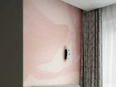 Modern bedroom with a large abstract blush pink mural wall, grey velvet headboard, dusty rose patterned bedding, and a sculptural white wall lamp.