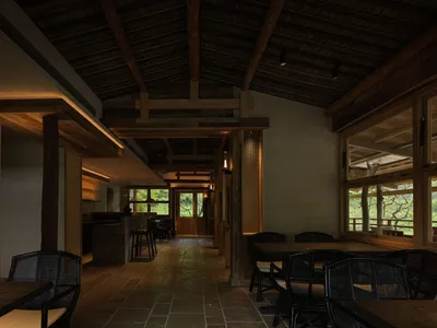 日式鄉村別墅餐廳內部，深色木質裸露梁柱、質感灰泥牆、石材地磚，以及黑色藤編餐椅環繞木桌的景象。