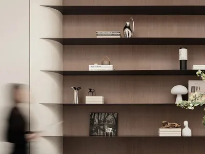Modern living room with dark walnut floating shelves displaying books, sculptures, and decorative objects against a light neutral wall, with a black console table in the foreground.