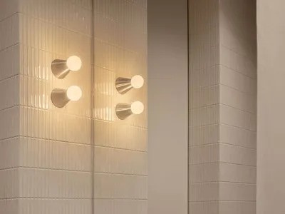 Modern bathroom featuring a thick Calacatta marble floating vanity with dramatic brown veining, paired with vertically ribbed white wall tiles and contemporary brushed-nickel wall sconces and faucet.