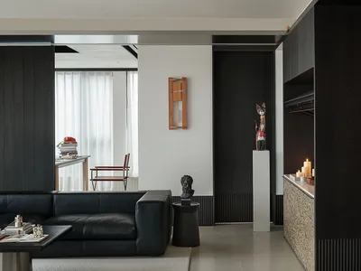 Modern monochrome living room with black leather sofa, black oak wall paneling, sculptural wooden cat figure on concrete pedestal, and built-in storage with patterned cabinet front.