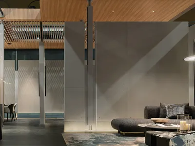 Modern minimalist living room featuring large concrete panels, warm wood slat ceiling, dark textured sofa, and sculptural floral arrangement on a black console.