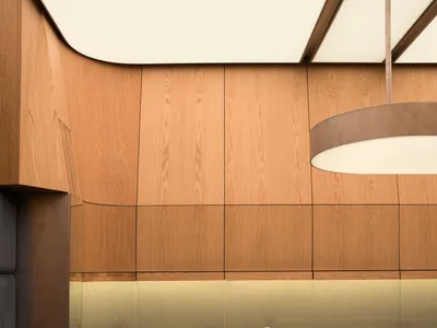 Interior view of a luxury jewelry store featuring curved oak wood paneling, dark green marble floor tiles, integrated backlit display cases, and a large circular pendant light hanging above a central curved glass display counter.
