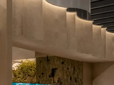 Modern lounge area featuring a curved textured plaster staircase, a large turquoise ocean wave mural, and a row of colorful mid-century modern lounge chairs in teal, red, pink, and orange.