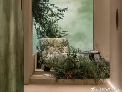 Modern minimalist living space featuring a sunken lounge chair surrounded by lush indoor plants, textured green plaster walls, and a large nature mural creating an indoor forest effect.