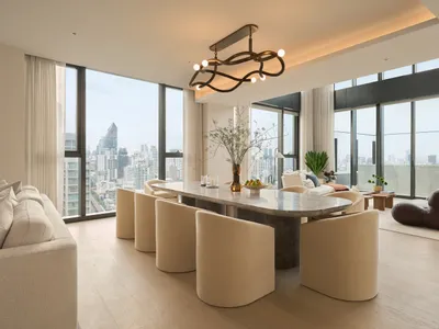 Modern open-plan dining area featuring a large curved marble table surrounded by cream boucle chairs, with floor-to-ceiling windows showcasing a dense city skyline.