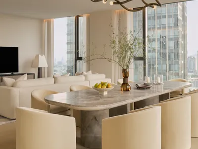 Modern luxury dining area featuring a large Calacatta marble table, six cream bouclé curved chairs, and an artistic bronze chandelier with floor-to-ceiling city views in the background.