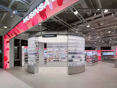 現代美妝店內部，設有大型半透明壓克力圓形香氛中島，搭配內建燈光，上方粉紅數位看板寫著MUSINSARA。