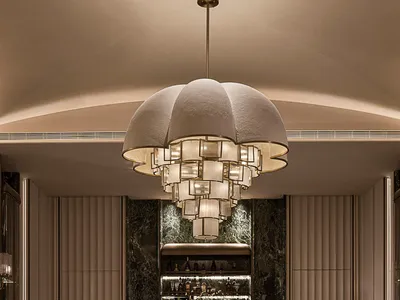 Luxurious formal dining room featuring a large round black marble table, velvet dining chairs, dramatic floral centerpiece, and a massive contemporary fabric chandelier against a dark green marble accent wall.