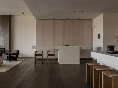 現代極簡開放式客餐廚空間，設有混凝土中島、淺色橡木系統櫃、深色橡木地板與木質雕塑感餐椅。