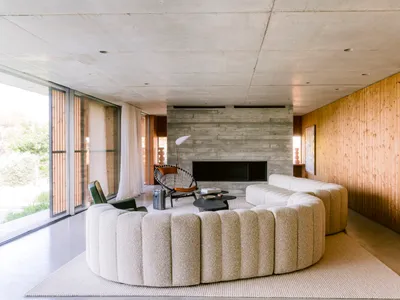 Modern living room featuring a large curved boucle sofa, concrete walls, vertical wood paneling, and a black woven accent chair in front of a fireplace.