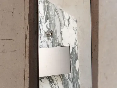 Close-up of a modern bathroom vanity mirror with white and green marble panel, stainless steel accessories, and raw concrete wall surround.