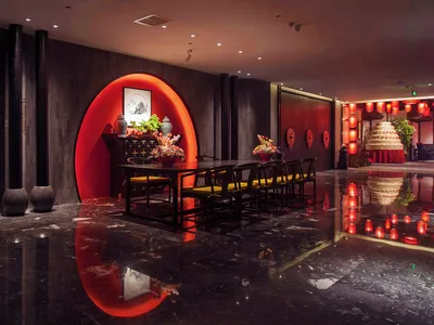 奢華中式餐廳內部，特色為發光的紅色圓拱、黑色大理石反光地板、深色木質牆面，以及搭配黃色絲綢椅子的傳統黑色餐桌。