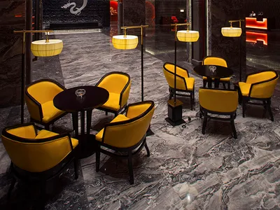 Luxurious hotel lobby featuring grey marble floors, yellow velvet armchairs, black tables, dramatic red ceiling panels, and a large white dragon mural on a black stone wall.