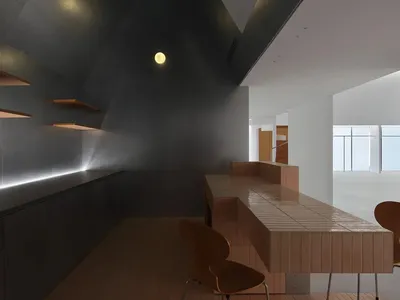 現代極簡風格餐廳，深色混凝土牆面、長型淺木色磁磚餐桌搭配嵌入式長椅、木椅，以及戲劇性的斜角建築線條。