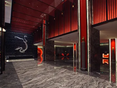 Luxurious hotel lobby featuring polished grey marble floors, dramatic red lacquered walls, a black stone dragon relief wall, and glowing red neon light installations.