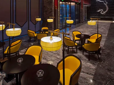 Luxurious hotel lobby lounge featuring bright yellow velvet armchairs, black round tables, dramatic red vertical slat walls, and grey marble flooring with a large white dragon mural in the background.
