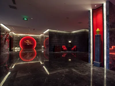Luxurious hotel lobby featuring polished black marble floors, dramatic red circular wall features, dark textured paneling, and red accent lighting.