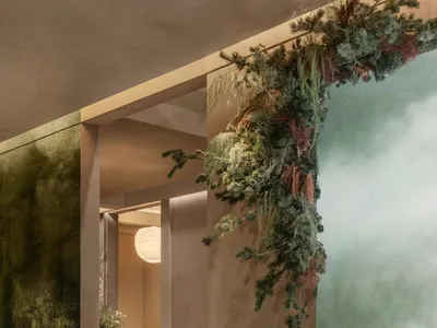 Modern biophilic lounge featuring a moss-textured chaise lounge, dark wood side table with open book, abundant hanging coniferous greenery, textured green wall, and a dining area visible in the background with blue velvet chairs.