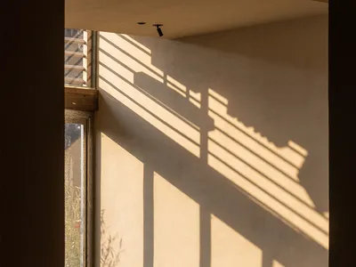寧靜的侘寂風餐廳，木製餐桌與藤編靠背椅，在溫暖陽光照射下，粗糙灰泥牆面呈現強烈的線性光影。