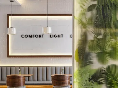 Modern cafe interior featuring walnut swivel chairs, grey upholstered booth seating, warm wood ceiling, and a glowing translucent green botanical partition wall.
