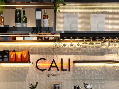 Modern cafe bar interior with grey textured tile wall, black countertop, grey bar stool, hanging wine glasses, and warm LED strip lighting.