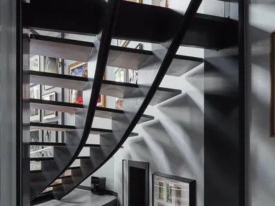 View of a modern black metal spiral staircase with wooden treads, a curved wood-paneled wall underneath, and a gallery wall of framed photographs on the right.
