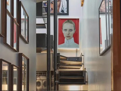 Modern black steel floating staircase with integrated lighting, flanked by dark wood framed portraits and a large red portrait of a woman at the top landing.