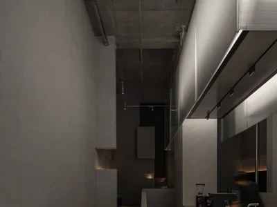粗獷風商業廚房的狹長走廊，左側為原始混凝土牆面，右側為深色地磚與線性LED燈光，一人正在操作義式咖啡機。