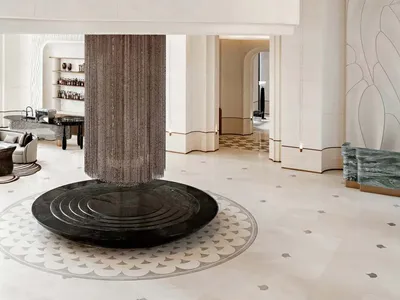 Expansive luxury hotel lobby featuring an enormous cascading crystal-bead chandelier hanging above a circular black marble base, with a curved mezzanine and light stone finishes.