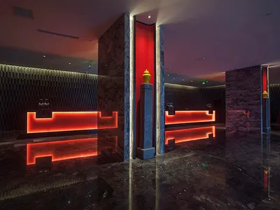 Luxurious hotel lobby interior with dark marble floors and walls, illuminated red reception desk, and dramatic architectural lighting.