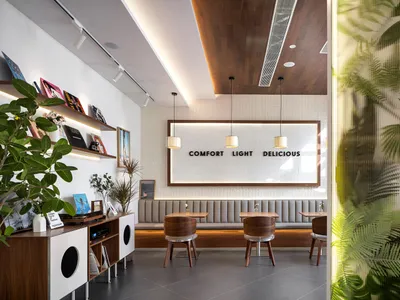 Modern cafe interior with wooden dining chairs, upholstered banquette seating, tropical leaf wallpaper, and a backlit sign reading COMFORT LIGHT DELICIOUS