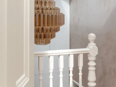 View of a modern white staircase with turned balusters, featuring a large amber acrylic tiered chandelier hanging from a skylight.