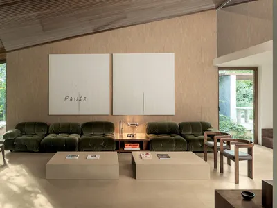 現代客廳展示兩組森林綠絨布模組沙發、米色石材茶几、溫暖木質壁板、大型抽象白色藝術品寫有PAUSE字樣，以及戶外茂密綠意景觀。