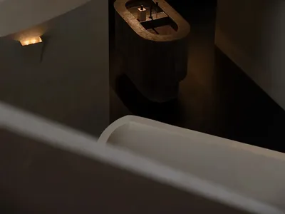 High-angle view of a minimalist dark bathroom featuring a freestanding concrete bathtub, recessed wall lighting, and dark flooring.