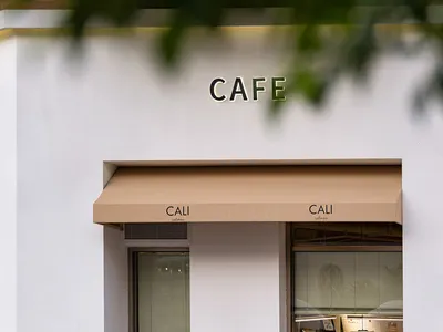 名為CALI的現代白色咖啡店街景，搭配米色遮陽棚、大面玻璃窗可見內部顧客，前方設有金屬欄杆。