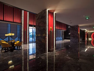 Luxurious hotel lobby featuring glossy black marble floors, bold red vertical wall panels, marble columns, and a sculptural red circular art installation in the background.
