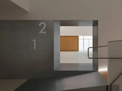 現代極簡混凝土樓梯與懸浮平台，通往設有木製櫃體的明亮上層展示空間