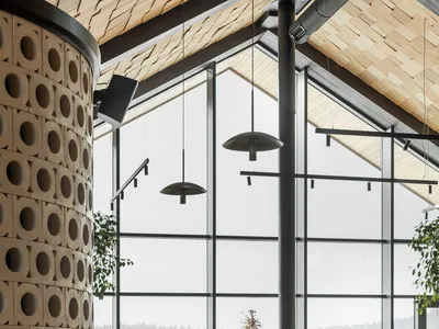 Modern restaurant interior with curved terracotta block column, dark wood dining tables, cream upholstered chairs, large windows showing snowy mountain view, and wooden ceiling.