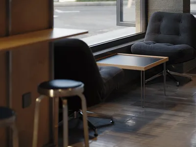 Modern corduroy lounge chair with chrome swivel base placed next to a large window with a wooden side table and black stool in foreground