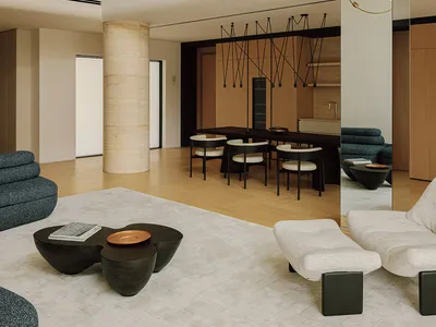 Modern double-height living room featuring a large cylindrical travertine column, light wood architectural volumes, sculptural brass and white pendant light, dark dining table with white chairs, and contemporary low seating in blue and cream tones.