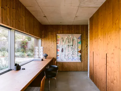 現代在家辦公室室內，包含垂直木質壁板、長型木桌、黑色皮椅、大型彩色抽象畫作，以及混凝土天花板與地板。