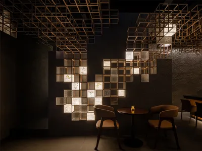 Modern restaurant interior featuring a large illuminated grid wall made of wooden cubes and textured glass panels with dried flowers, paired with round wooden tables and tan leather chairs under a dramatic geometric ceiling installation.