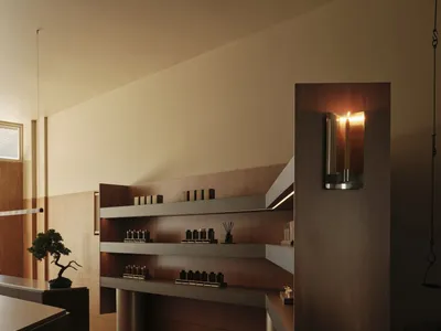 Modern minimalist interior featuring a floating walnut wood console with integrated shelves, terracotta floor tiles, and warm wall sconce lighting.