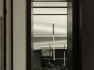 從玄關透過深色木門框望向現代簡約餐廳，室內有深色餐桌、皮革餐椅、吊燈與大型樹枝雕塑花器。