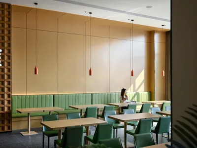Modern restaurant interior with green leather booths, matching green chairs, light wood tables, and a prominent wooden lattice feature wall with hanging red pendant lights.