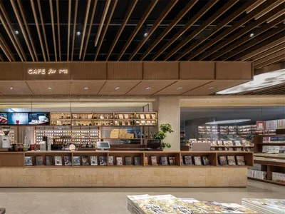 現代書店咖啡廳室內，設有長型洞石與木質服務吧台、線型木格柵天花板、溫暖中性色調，以及整合式書籍陳列。